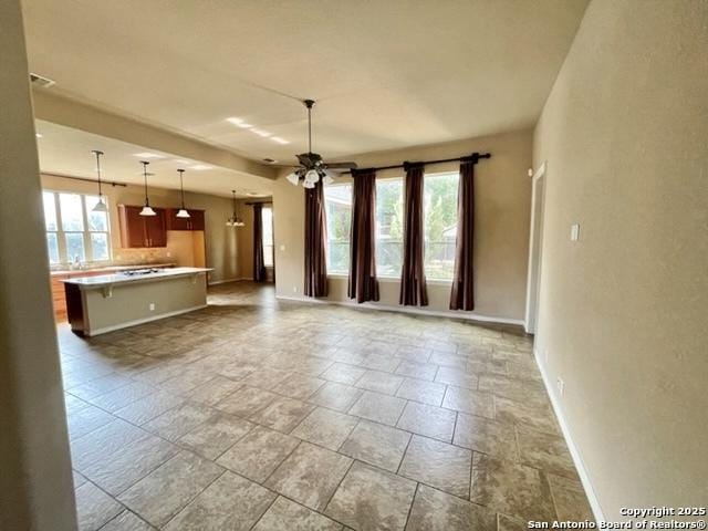 interior space with baseboards, ceiling fan, open floor plan, light countertops, and pendant lighting