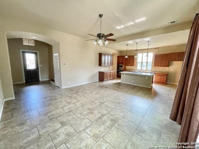 kitchen featuring arched walkways, brown cabinets, backsplash, and light countertops