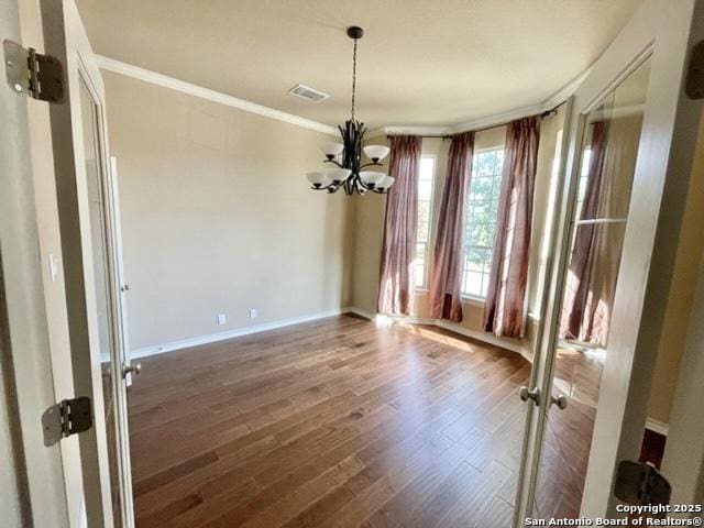 unfurnished dining area featuring visible vents, baseboards, wood finished floors, an inviting chandelier, and crown molding