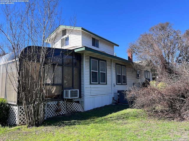 view of side of home with a wall unit AC, a sunroom, cooling unit, and a lawn