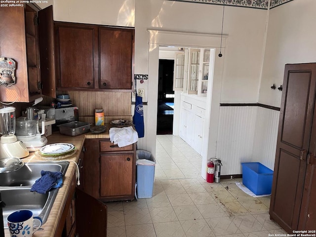 kitchen with light floors, light countertops, wainscoting, dark brown cabinetry, and a sink