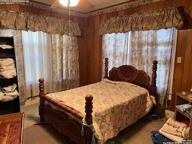 carpeted bedroom featuring wood walls and a ceiling fan