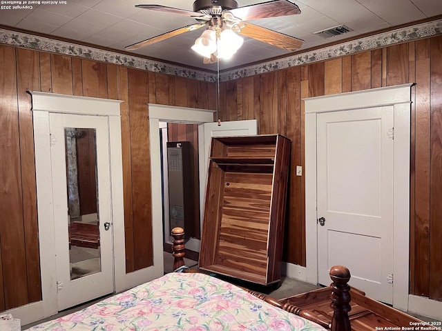 bedroom with a ceiling fan, visible vents, and wood walls