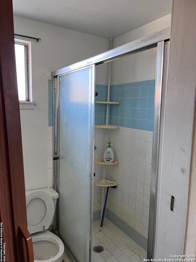 bathroom with a textured ceiling, a stall shower, and toilet