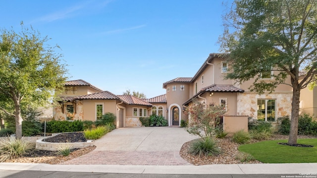 mediterranean / spanish-style home with driveway, stone siding, stucco siding, and a tiled roof