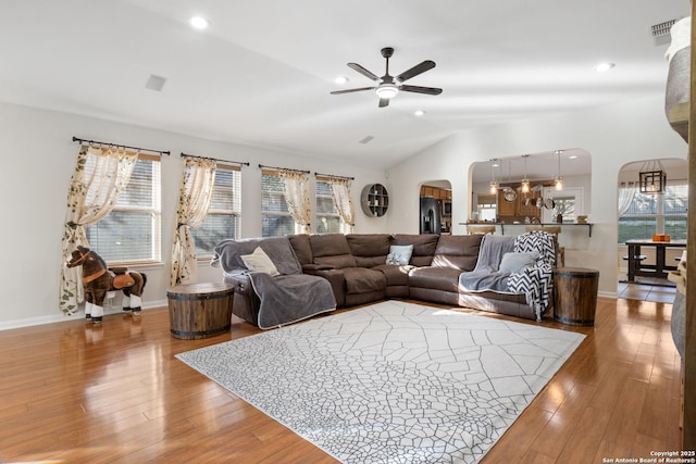 living room featuring arched walkways, wood-type flooring, a healthy amount of sunlight, and lofted ceiling