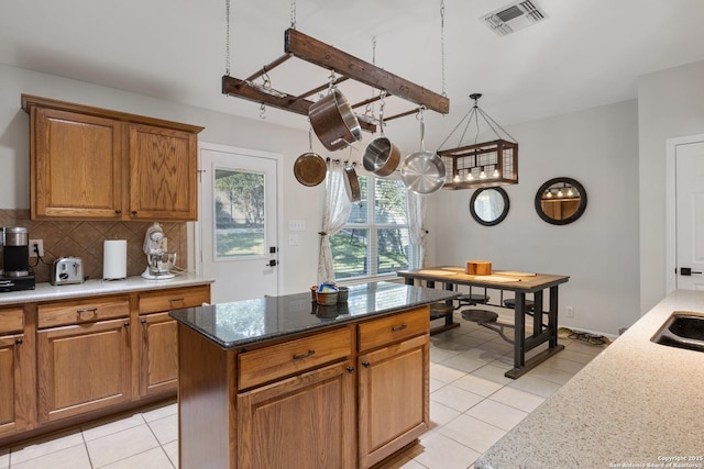 kitchen featuring brown cabinetry, visible vents, decorative backsplash, and light stone countertops