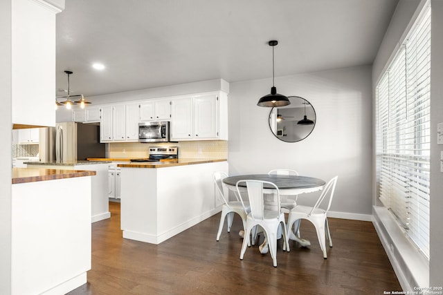 kitchen featuring dark wood-style flooring, a peninsula, stainless steel appliances, white cabinetry, and wooden counters