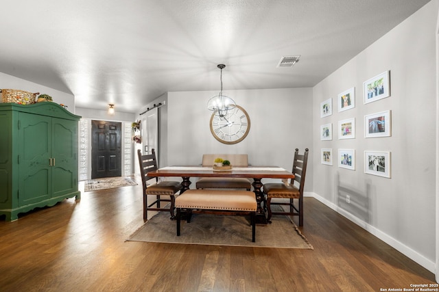 dining space featuring dark wood finished floors, visible vents, an inviting chandelier, a barn door, and baseboards