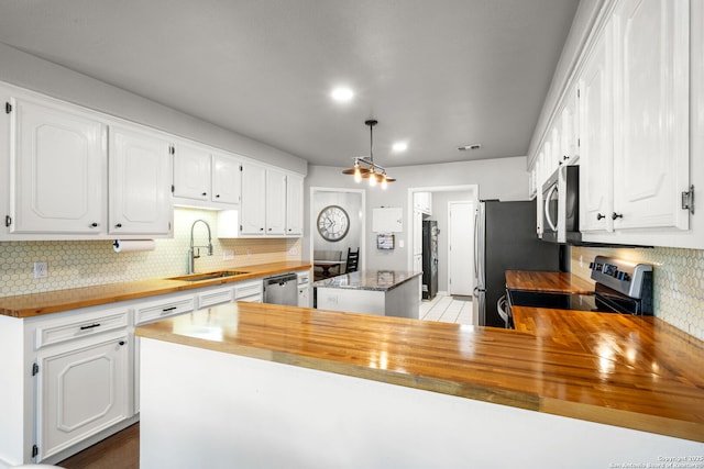 kitchen featuring a center island, stainless steel appliances, wooden counters, white cabinetry, and a sink