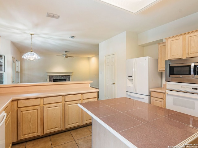 kitchen with white appliances, ceiling fan with notable chandelier, light tile patterned flooring, light brown cabinetry, and a high end fireplace