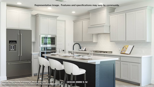 kitchen featuring a center island with sink, appliances with stainless steel finishes, light countertops, and backsplash