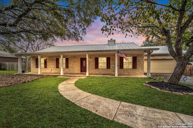 ranch-style house featuring metal roof, an attached garage, fence, stone siding, and a standing seam roof