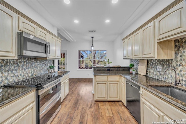 kitchen with stainless steel appliances, a peninsula, a sink, visible vents, and light wood finished floors