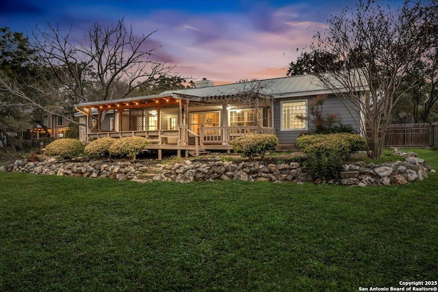 back of property at dusk with a yard, a chimney, a wooden deck, and fence