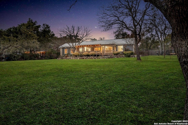 back of house at dusk featuring a lawn and fence