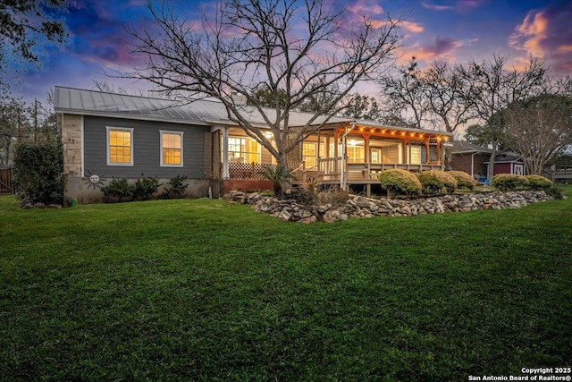 back of house at dusk with a standing seam roof, metal roof, and a lawn