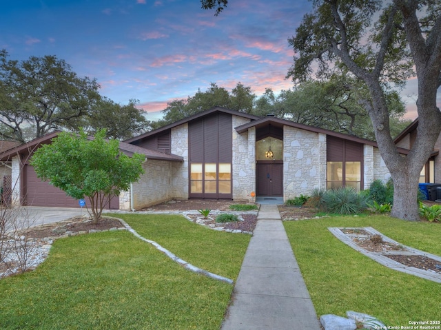 mid-century inspired home with a garage, stone siding, a lawn, and concrete driveway