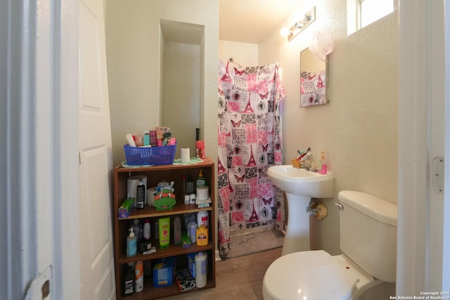 bathroom featuring a shower with shower curtain, a textured wall, toilet, and wood finished floors