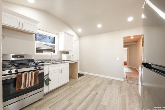 kitchen featuring white microwave, vaulted ceiling, a sink, gas range, and light wood-type flooring