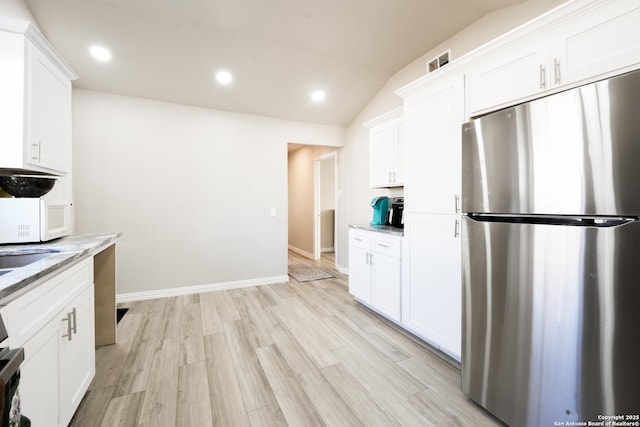 kitchen with light stone counters, white microwave, white cabinetry, vaulted ceiling, and freestanding refrigerator