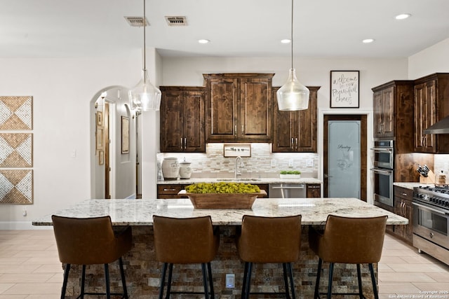 kitchen with dark brown cabinetry, arched walkways, a sink, stainless steel appliances, and backsplash