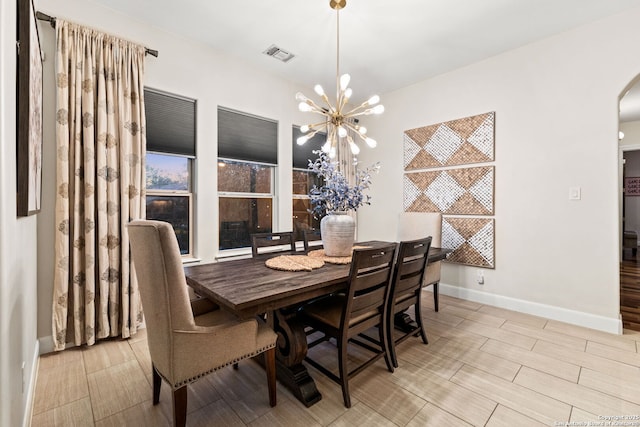 dining space with arched walkways, a notable chandelier, visible vents, baseboards, and wood tiled floor