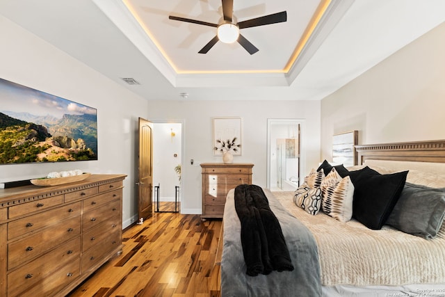 bedroom with light wood-style flooring, a ceiling fan, visible vents, baseboards, and a tray ceiling