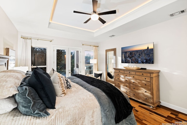 bedroom with french doors, a raised ceiling, visible vents, wood finished floors, and access to outside