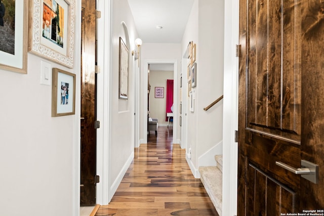 hall with a barn door, stairway, wood finished floors, and baseboards