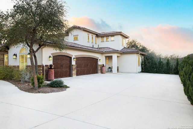 mediterranean / spanish-style home with driveway, an attached garage, a tiled roof, and stucco siding