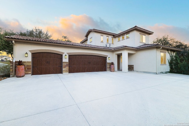 mediterranean / spanish home with a garage, concrete driveway, a tiled roof, and stucco siding