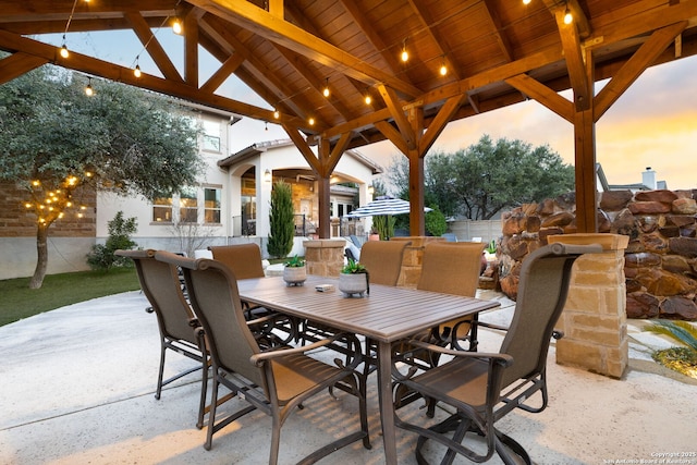 patio terrace at dusk with fence, outdoor dining area, and a gazebo