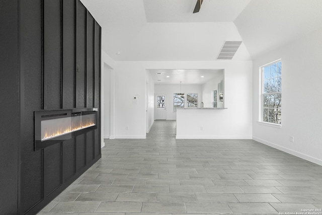 unfurnished living room with a healthy amount of sunlight, ceiling fan, lofted ceiling, and a glass covered fireplace