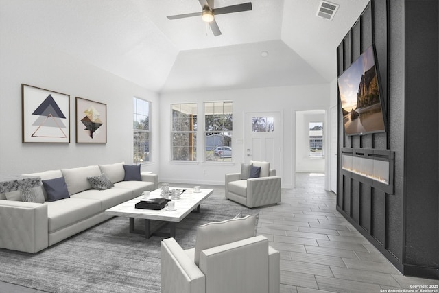 living room with a large fireplace, visible vents, vaulted ceiling, and ceiling fan