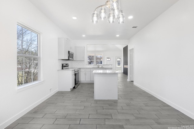 kitchen with stainless steel appliances, backsplash, white cabinets, a kitchen island, and a sink