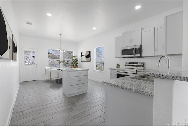 kitchen with a sink, light stone countertops, stainless steel appliances, pendant lighting, and backsplash