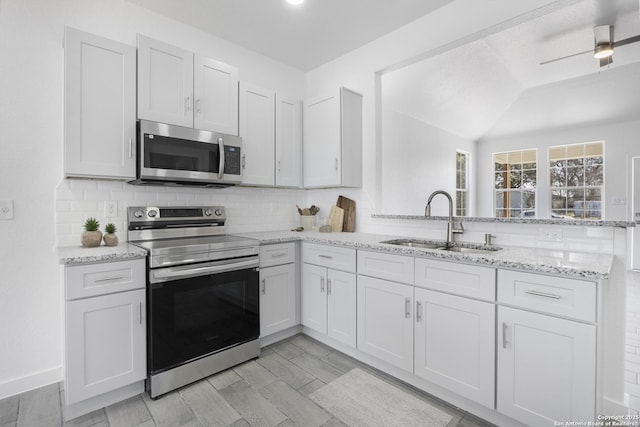 kitchen with light stone counters, a peninsula, a sink, appliances with stainless steel finishes, and tasteful backsplash