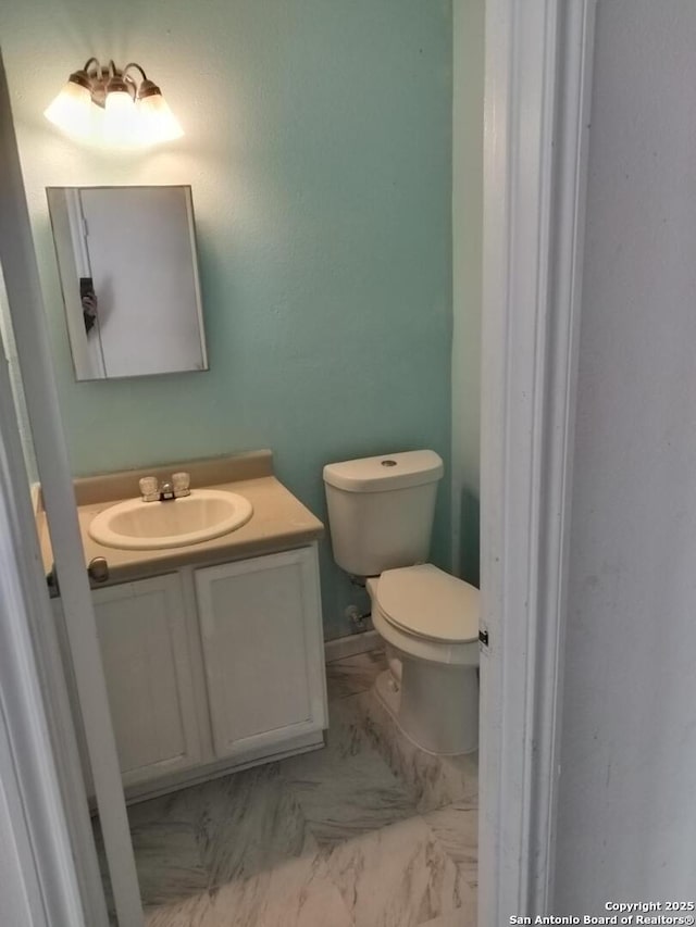 half bath with marble finish floor, vanity, and toilet