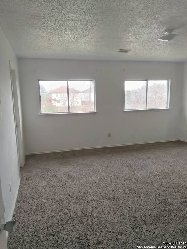 empty room with carpet floors, visible vents, a textured ceiling, and baseboards