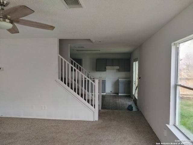 stairway with a textured ceiling, carpet floors, visible vents, and a ceiling fan