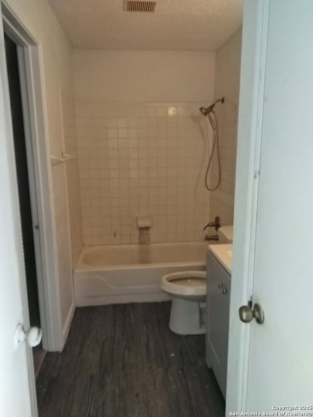 full bathroom featuring toilet, wood finished floors, a textured ceiling, vanity, and washtub / shower combination