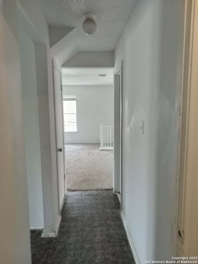 corridor featuring a textured ceiling, dark colored carpet, and visible vents