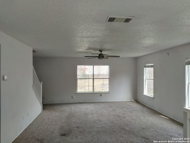 unfurnished room with a textured ceiling, visible vents, a ceiling fan, stairway, and carpet