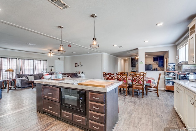 kitchen featuring black microwave, visible vents, open floor plan, dark brown cabinets, and ornamental molding