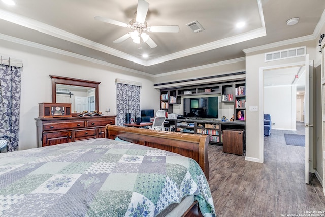 bedroom featuring ornamental molding, a tray ceiling, wood finished floors, and visible vents