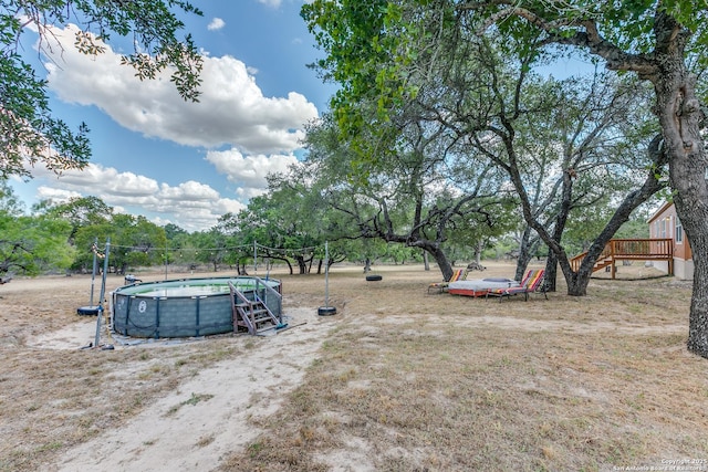 view of yard featuring a trampoline, an outdoor pool, and a deck