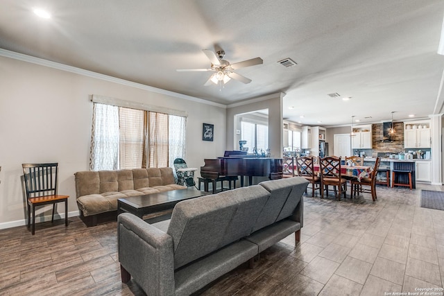 living room with a ceiling fan, visible vents, ornamental molding, and baseboards