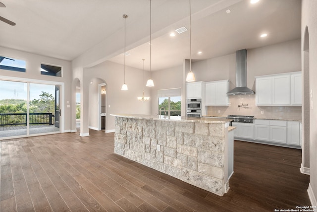 kitchen featuring a towering ceiling, visible vents, wall chimney exhaust hood, tasteful backsplash, and dark wood finished floors