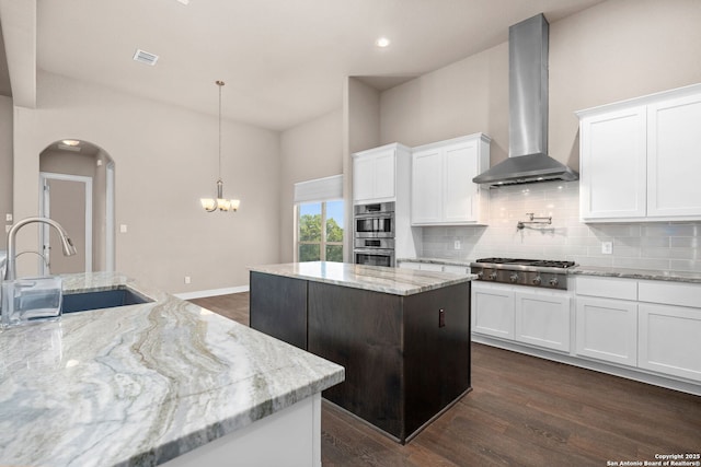 kitchen with decorative backsplash, wall chimney exhaust hood, a kitchen island, appliances with stainless steel finishes, and a sink